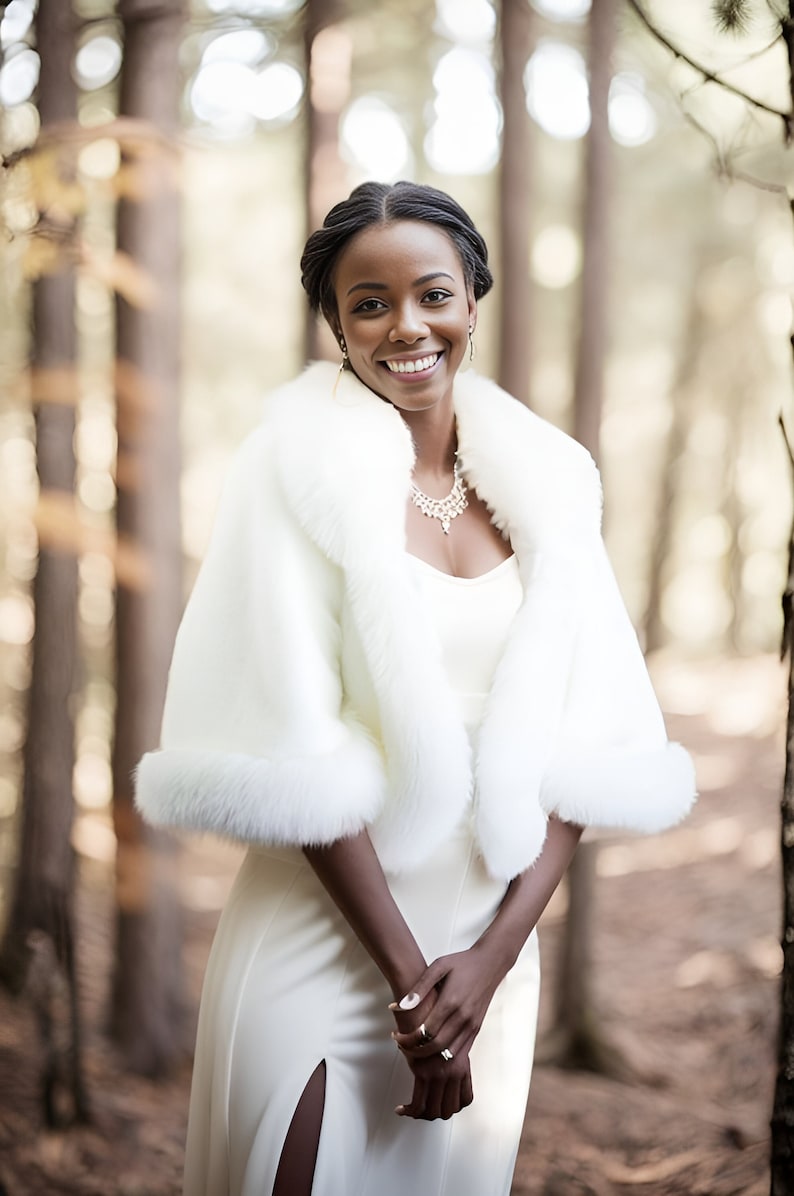 May include: A bride wearing a white fur shawl with a white dress and a silver necklace. She is standing in a forest.