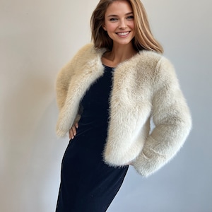 May include: A woman wearing a white faux fur jacket over a black velvet dress. She is smiling and looking at the camera.