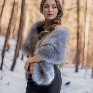 May include: A woman wearing a gray faux fur shawl over a black dress, standing in a snowy forest.
