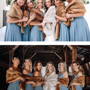 May include: A group of bridesmaids wearing blue dresses and brown faux fur wraps stand in a snowy outdoor setting. The bride is in the center wearing a white dress and a white faux fur wrap.