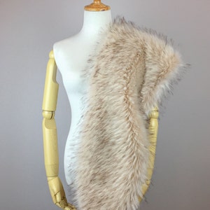 May include: A beige faux fur scarf draped over a white mannequin. The scarf is soft and fluffy, with a long, flowing design.