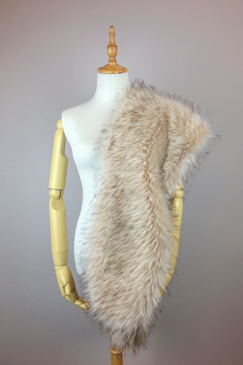 May include: A beige faux fur scarf draped over a white mannequin. The scarf is soft and fluffy, with a long, flowing design.