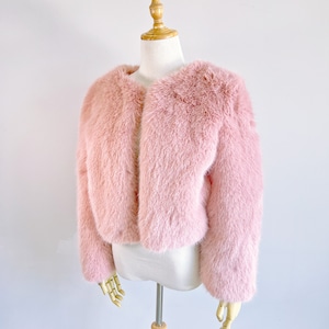 May include: A pink faux fur jacket with a cropped length and long sleeves. The jacket is displayed on a white mannequin.