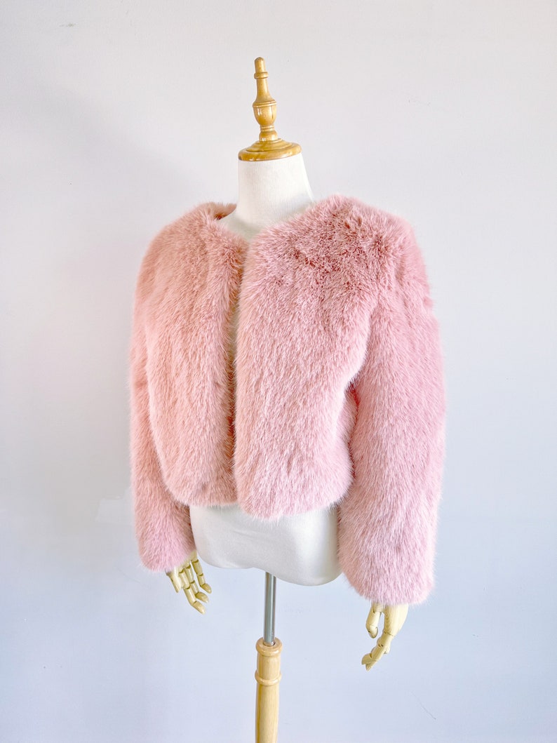 May include: A pink faux fur jacket with a cropped length and long sleeves. The jacket is displayed on a white mannequin.