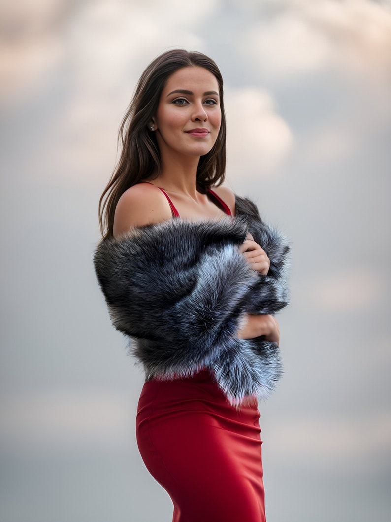 May include: A woman wearing a red dress with a black and white fur shawl. She is standing in front of a cloudy sky.