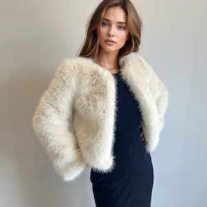 May include: A white faux fur jacket with a cropped length and long sleeves. The jacket is worn over a black dress.