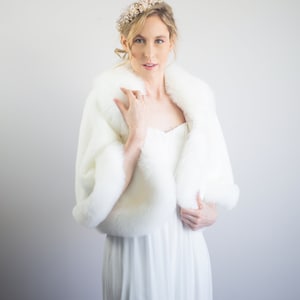 May include: A white faux fur shawl with a long white dress. The woman is wearing a gold and white beaded headband.