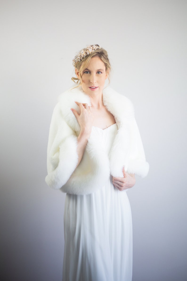 May include: A white faux fur shawl with a long white dress. The woman is wearing a gold and white beaded headband.