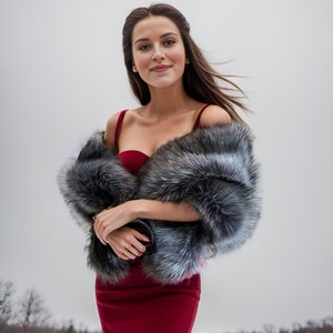 May include: A woman wearing a red dress with a fur shawl. She is standing in a snowy field with trees in the background.