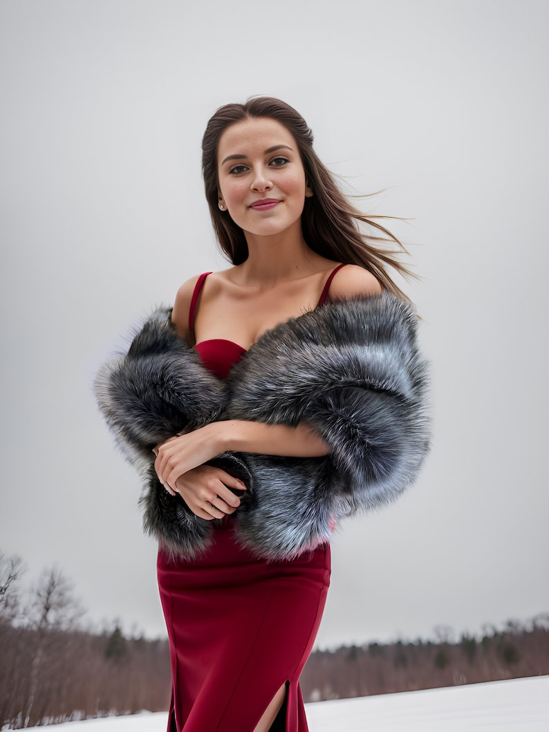 May include: A woman wearing a red dress with a fur shawl. She is standing in a snowy field with trees in the background.
