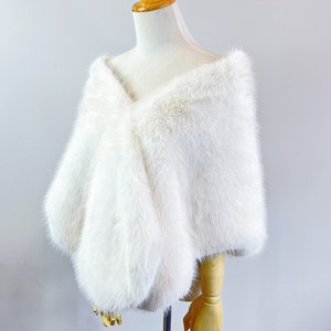 May include: White faux fur shawl draped over a dress form. The shawl is made of soft, fluffy fur and has a simple, elegant design.