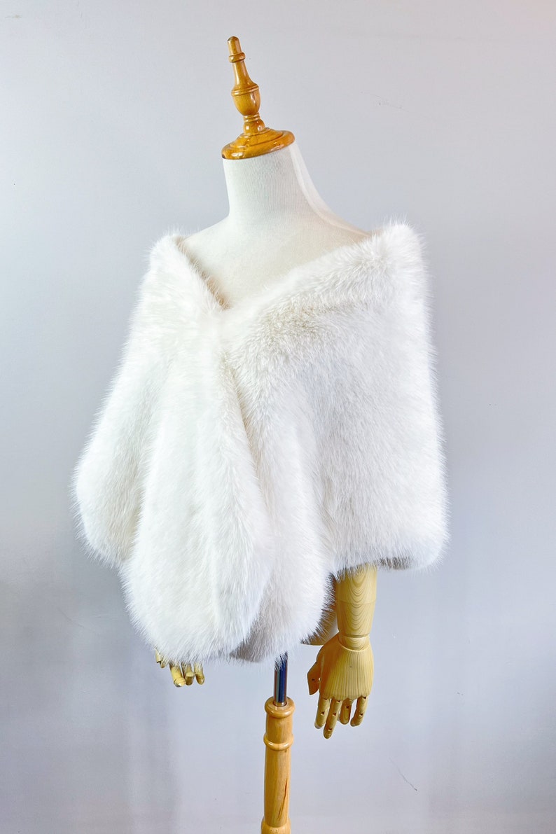 May include: White faux fur shawl draped over a dress form. The shawl is made of soft, fluffy fur and has a simple, elegant design.