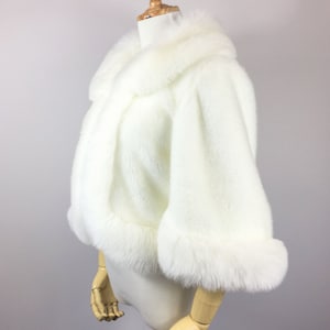 May include: A white faux fur shrug with a collar and long sleeves. The shrug is on a white mannequin.