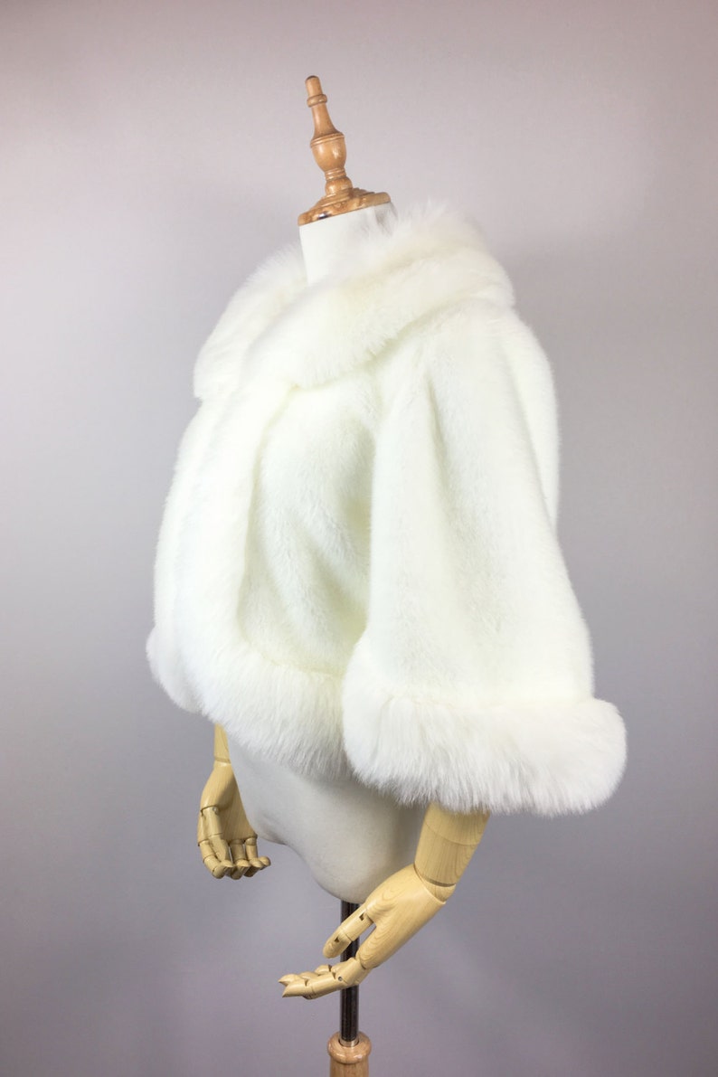 May include: A white faux fur shrug with a collar and long sleeves. The shrug is on a white mannequin.