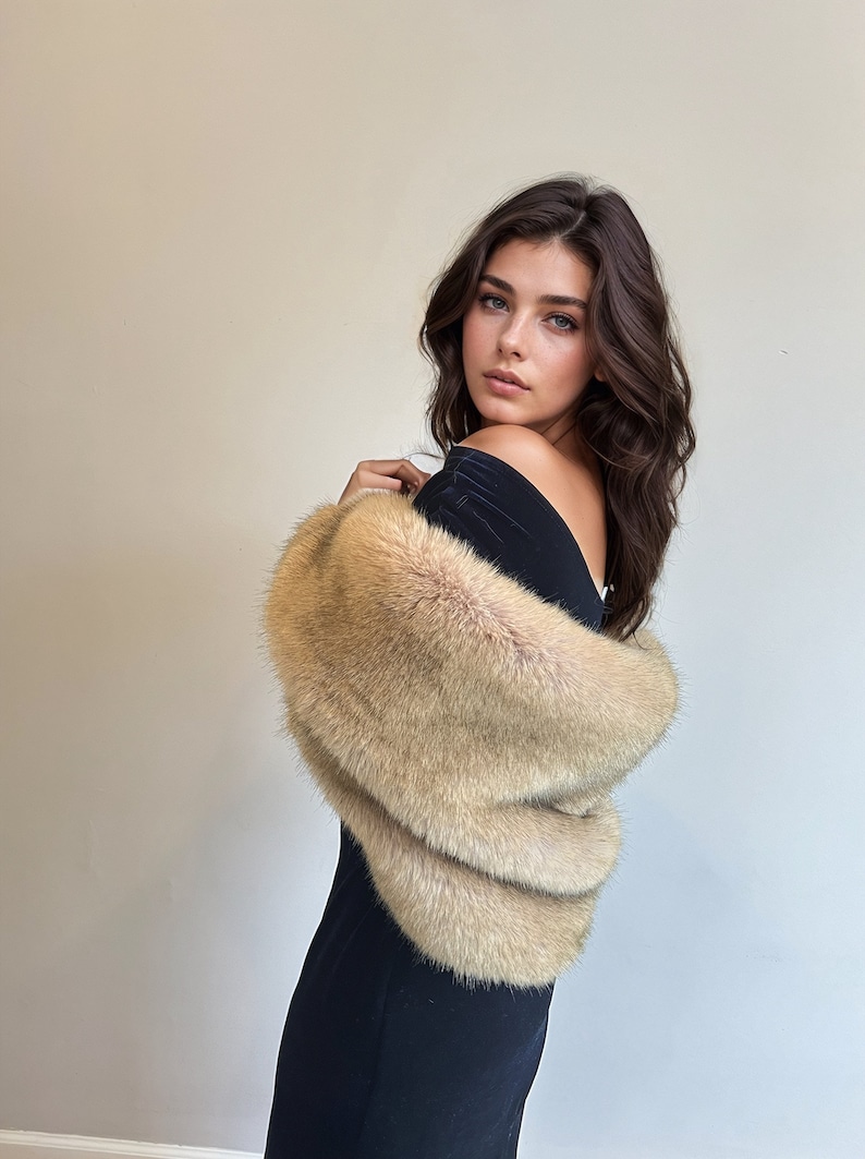 May include: A woman wearing a black dress with a beige fur shawl draped over her shoulders.