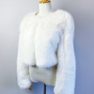 May include: A white faux fur cropped jacket with long sleeves.