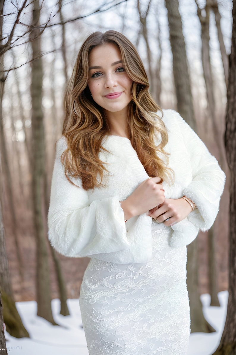 May include: A woman wearing a white faux fur shrug over a white lace dress. She is standing in a snowy forest.