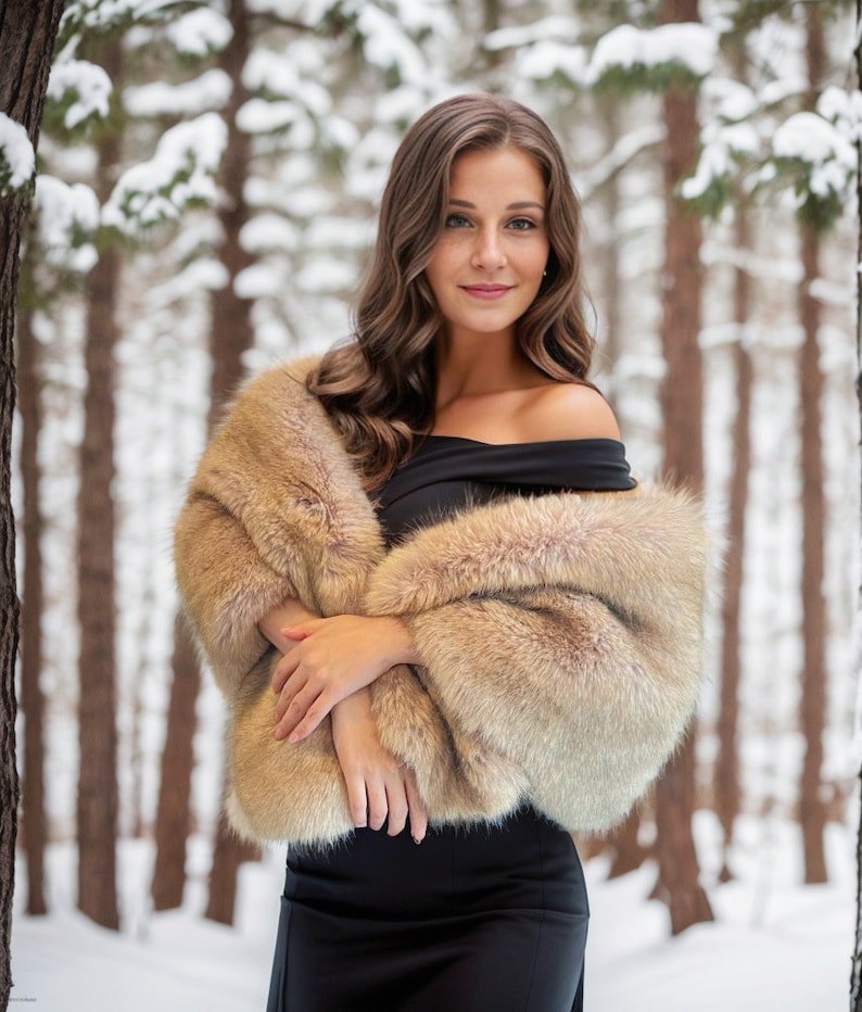 May include: A woman wearing a brown fur shawl over a black off-the-shoulder dress. She is standing in a snowy forest.