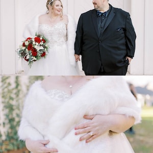 May include: A bride and groom are standing outside on their wedding day. The bride is wearing a white wedding dress with a white fur shawl and a bouquet of red roses. The groom is wearing a black suit with a black bow tie.