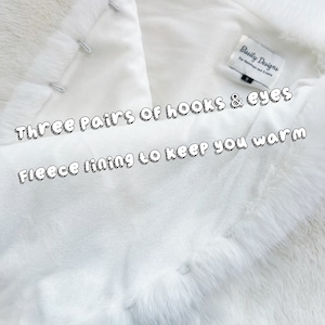 May include: White faux fur shawl with a fleece lining. The shawl has three pairs of hooks and eyes for closure. The label reads "Sisily Designs for Weddings and Events".