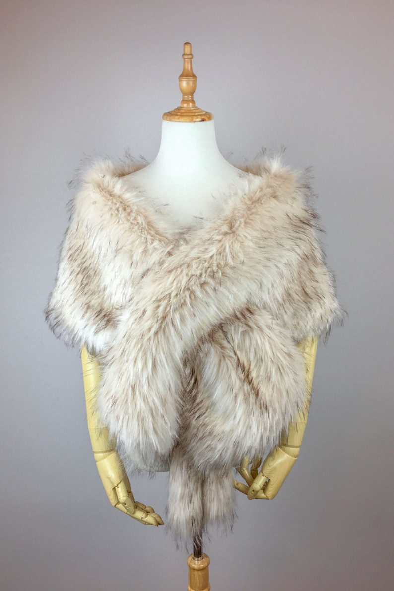 May include: A faux fur shawl in a light brown and white color. The shawl is draped over a mannequin and has a soft, fluffy texture.