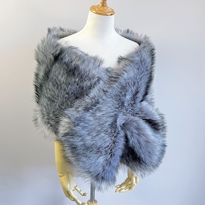 May include: A gray faux fur shawl with a soft, fluffy texture. The shawl is draped over a mannequin and is perfect for adding a touch of elegance to any outfit.