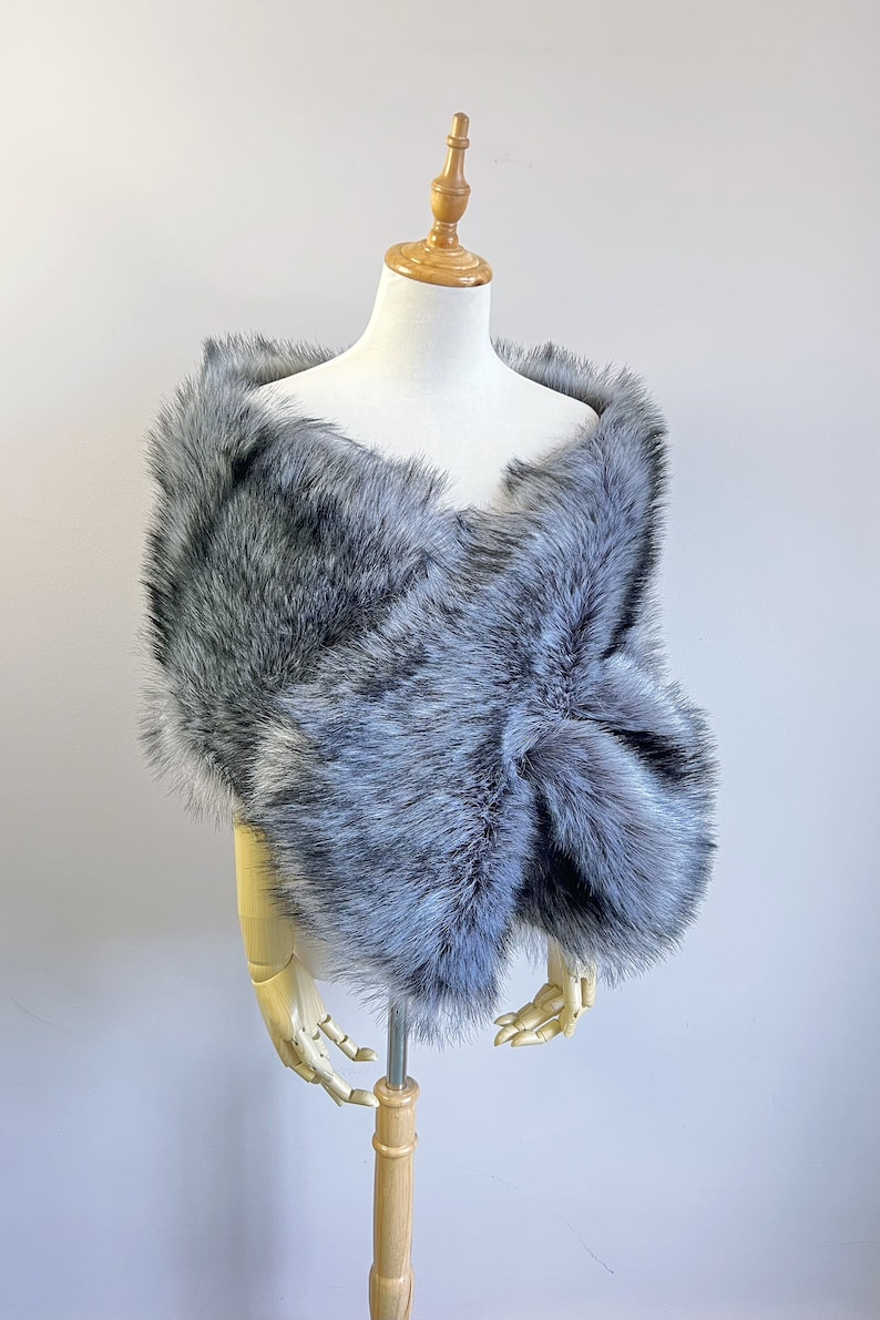 May include: A gray faux fur shawl with a soft, fluffy texture. The shawl is draped over a mannequin and is perfect for adding a touch of elegance to any outfit.
