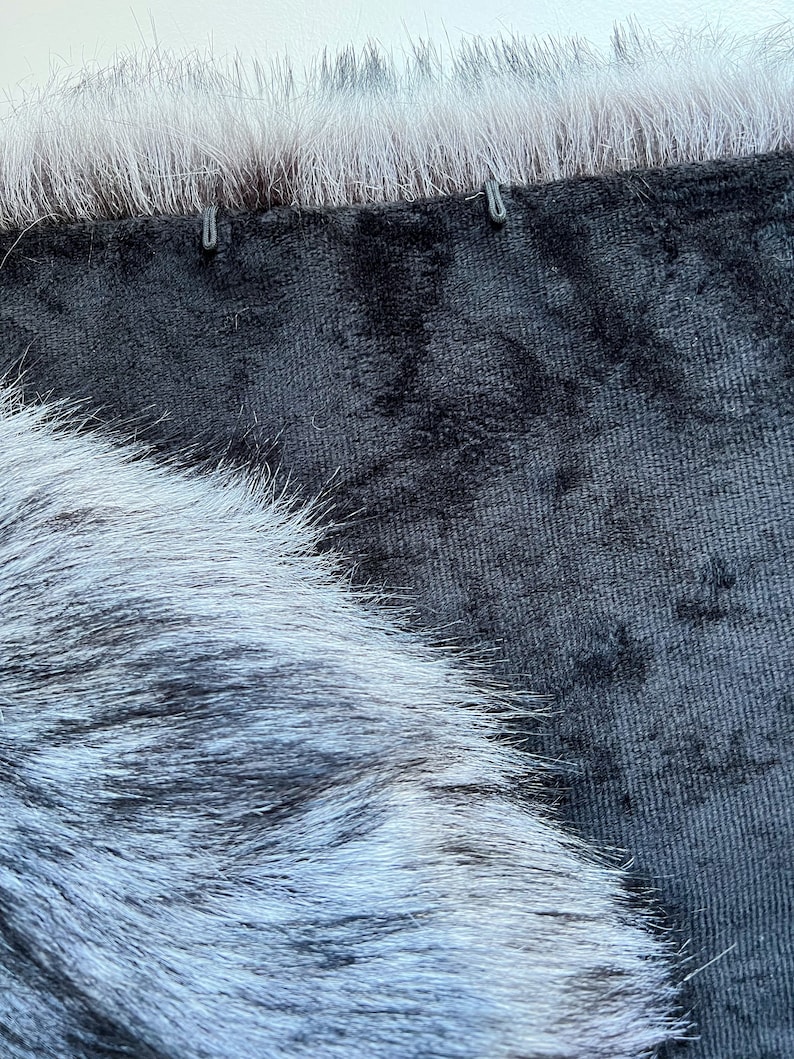 May include: Close-up of a black velvet fabric with a white fur trim. The fur is soft and fluffy, and the velvet is smooth and luxurious.