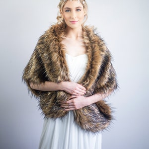 May include: A woman wearing a white dress with a brown faux fur shawl. She is wearing a gold headband with small white flowers.