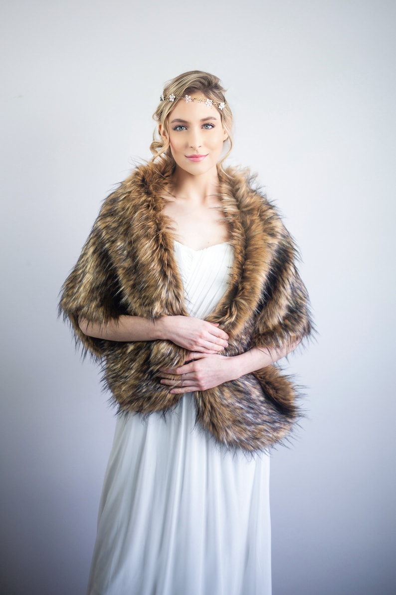 May include: A woman wearing a white dress with a brown faux fur shawl. She is wearing a gold headband with small white flowers.