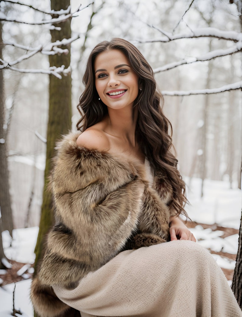 May include: A woman wearing a brown faux fur shawl over a beige dress, sitting in a snowy forest. She is smiling and looking at the camera.