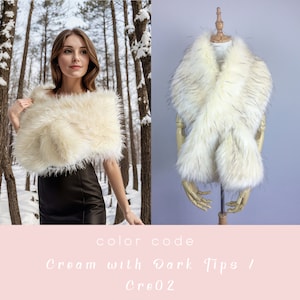 May include: Cream colored faux fur shawl with dark tips. The shawl is draped over a mannequin and a person wearing a black dress. The color code is "Cre02".
