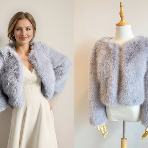May include: A light gray faux fur shrug with a cropped length. The shrug is open in the front and has long sleeves.