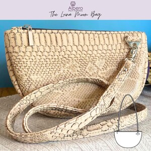 May include: A beige, snake-skin patterned Luna Moon Bag with a silver zipper and strap hardware. The bag has a detachable strap and a curved shape. The text "Albero Patterns" and "The Luna Moon Bag" are visible on the image.