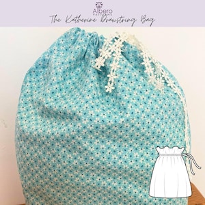 May include: A blue drawstring bag with a white floral pattern and white lace trim. The bag has a drawstring closure and the text "The Katherine Drawstring Bag" is visible.