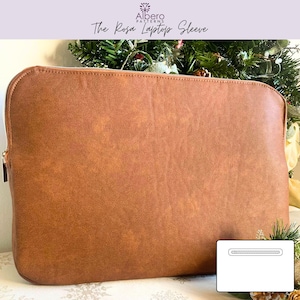 May include: A brown laptop sleeve with a zip closure. The sleeve has a textured surface and the text "The Rosa Laptop Sleeve" is visible. The sleeve is designed to protect a laptop.