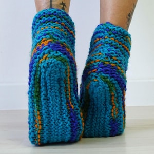 May include: A pair of ankle-length hand-knitted socks featuring a chunky yarn texture. The socks are crafted from a variegated blend of bright turquoise, deep royal blue, forest green, and vibrant orange yarn in a thick, ribbed knit pattern.