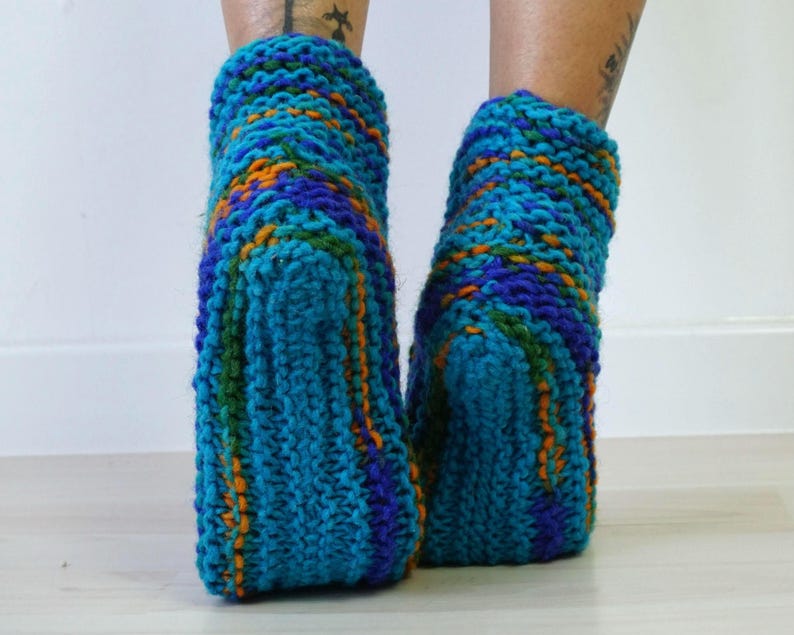 May include: A pair of ankle-length hand-knitted socks featuring a chunky yarn texture. The socks are crafted from a variegated blend of bright turquoise, deep royal blue, forest green, and vibrant orange yarn in a thick, ribbed knit pattern.