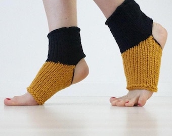 May include: A pair of open-heel yoga socks featuring a ribbed knit texture. The upper section around the ankle is solid black, while the lower section covering the midfoot is a mustard yellow colour. These socks leave the toes and heels exposed.