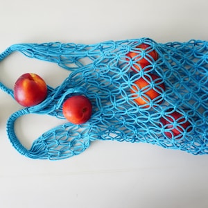 May include: A bright blue, hand-knitted net bag filled with ripe nectarines. The bag has two handles and a diamond-patterned weave. Three nectarines are outside the bag. The fruit is red with yellow and orange hues.