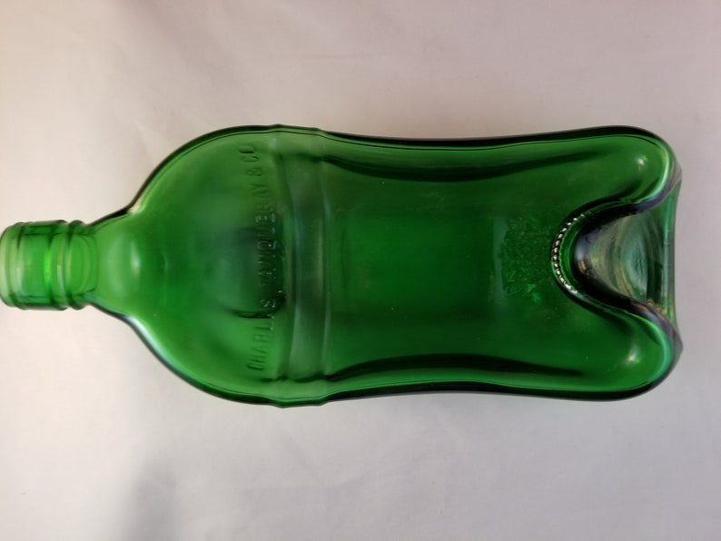 May include: A green glass bottle with a unique shape and a label that reads "Charles S. Welch & Co."