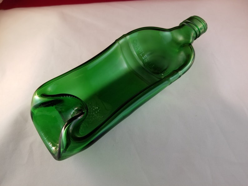 May include: A green glass bottle that has been repurposed into a decorative dish. The bottle has been cut and shaped to create a unique and functional piece.