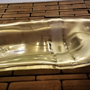 May include: A clear glass bottle that has been repurposed into a decorative dish. The bottle has been cut and shaped to create a unique and functional piece.