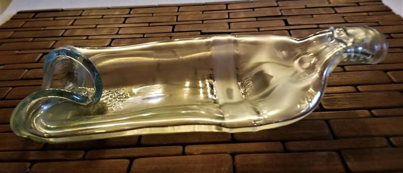 May include: A clear glass bottle that has been repurposed into a decorative dish. The bottle has been cut and shaped to create a unique and functional piece.