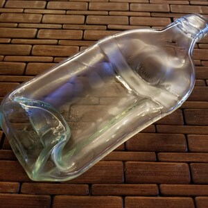 May include: A clear glass bottle with a slightly curved shape, lying on a brown woven surface.