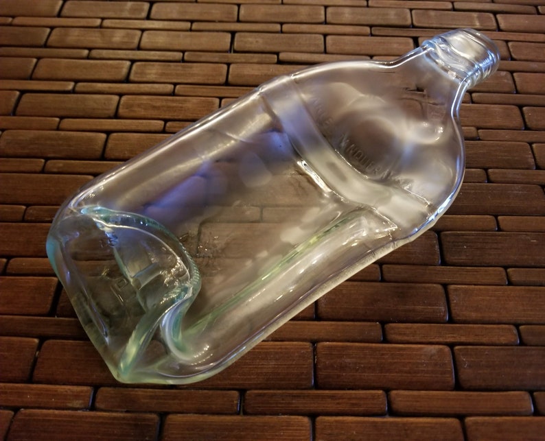 May include: A clear glass bottle with a slightly curved shape, lying on a brown woven surface.