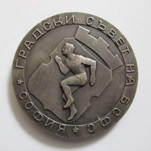 Può includere: Una medaglia d'argento con una figura che corre al centro. La medaglia è incisa con il testo "ГРАДСКИ СЪВЕТ НА СОФИЯ" in cirillico.