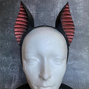 May include: Black headband with red and black devil horns. The horns are textured and have a pointed tip.