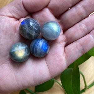 May include: Four iridescent labradorite spheres in various shades of blue and green, held in a hand.