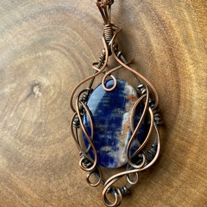 May include: A copper wire wrapped pendant featuring a blue and white gemstone. The pendant is attached to a copper chain.